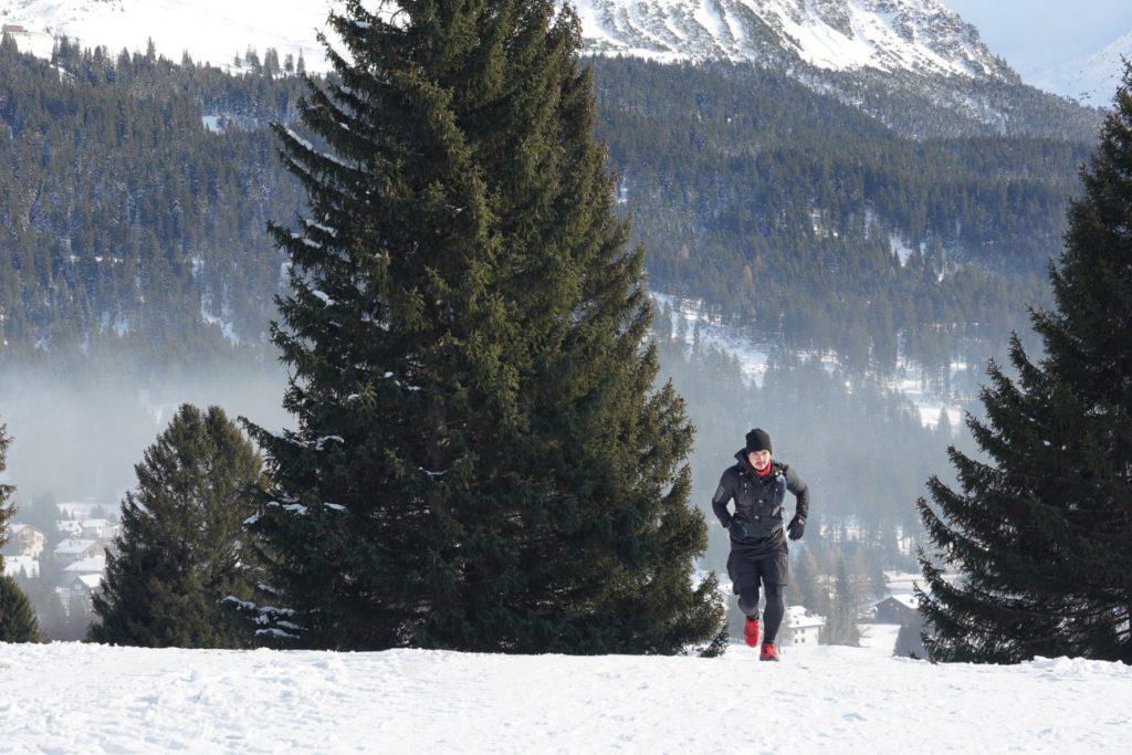 Trailrunner mit Icebug Arcus BUGrip GTX auf einer Schneepiste im Aufstieg mit Bergen im Hintergrund
