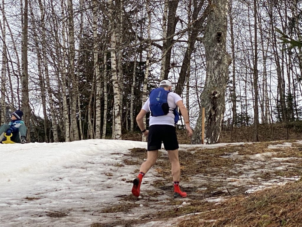 Läufer mit deuter Ascender 13 Rucksack auf einem teils schneebedeckten Trail