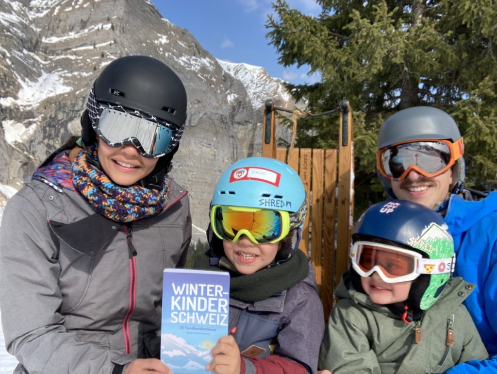 Familie beim Schlitteln im Schweizer Winter mit dem Winterkinder Schweiz Buch
