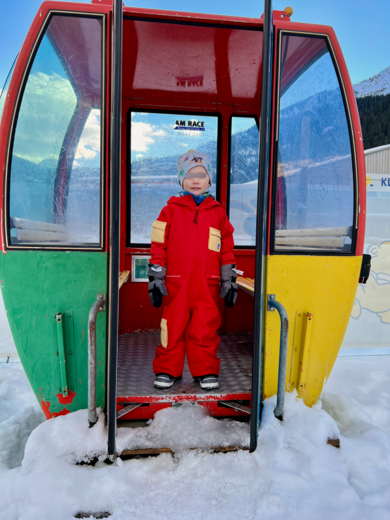 Kind im roten namuk Quest Skianzug in einer alten, bunten Gondel