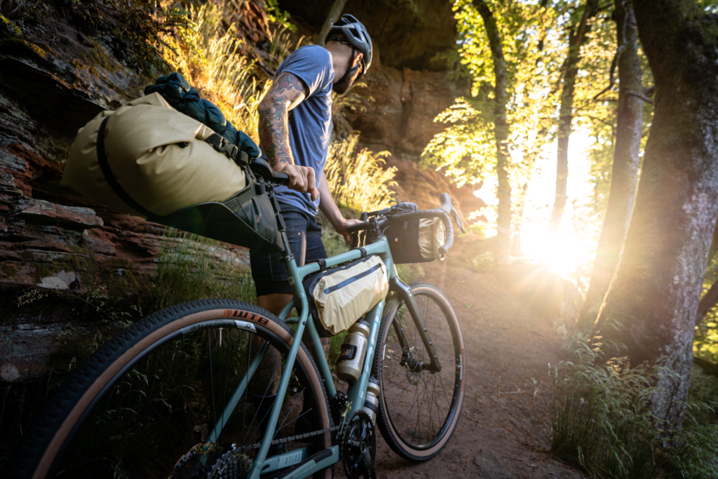 Bikepacker im Wald mit Gegelicht und deuter Bikepacking Taschen – Modell Cabezon SB 16 L – Saddle Pack / Satteltasche