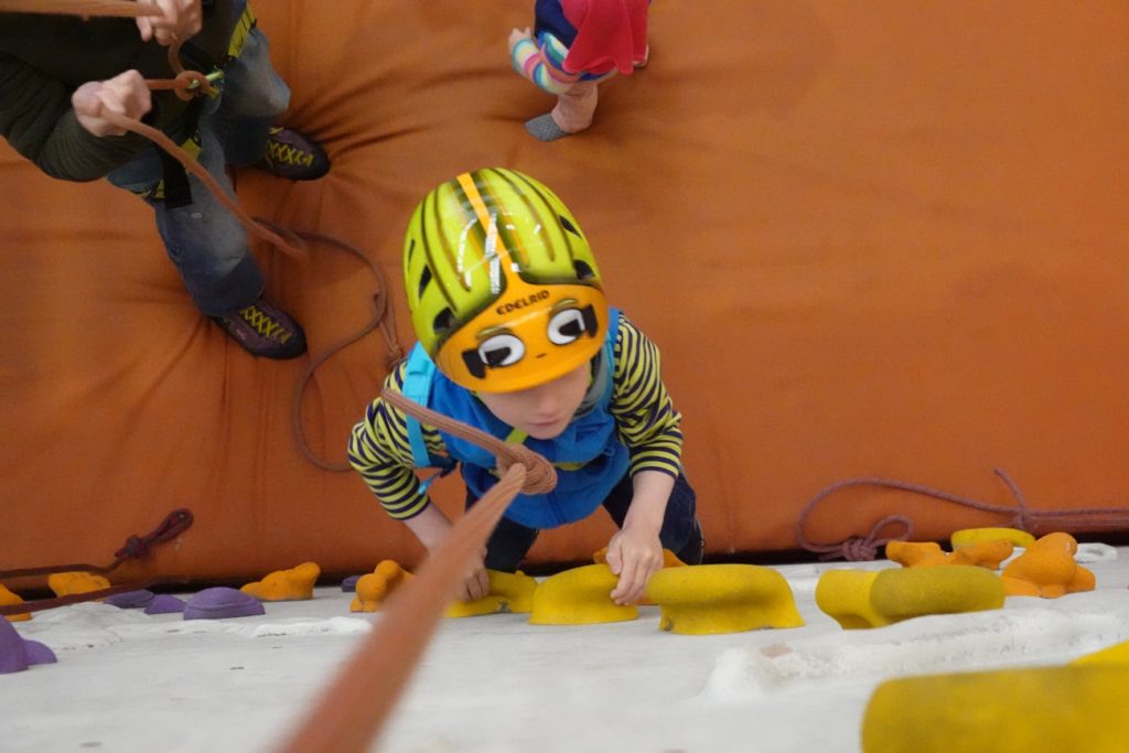 Junge trägt Edelrid Kids Shield Helm an der Kletterwand mit Seil Toprope gesichert