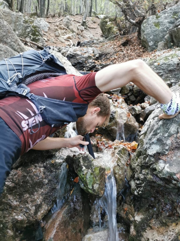Trailrunner trinkt mit LifeStraw Peak Series Straw aus einem Bach