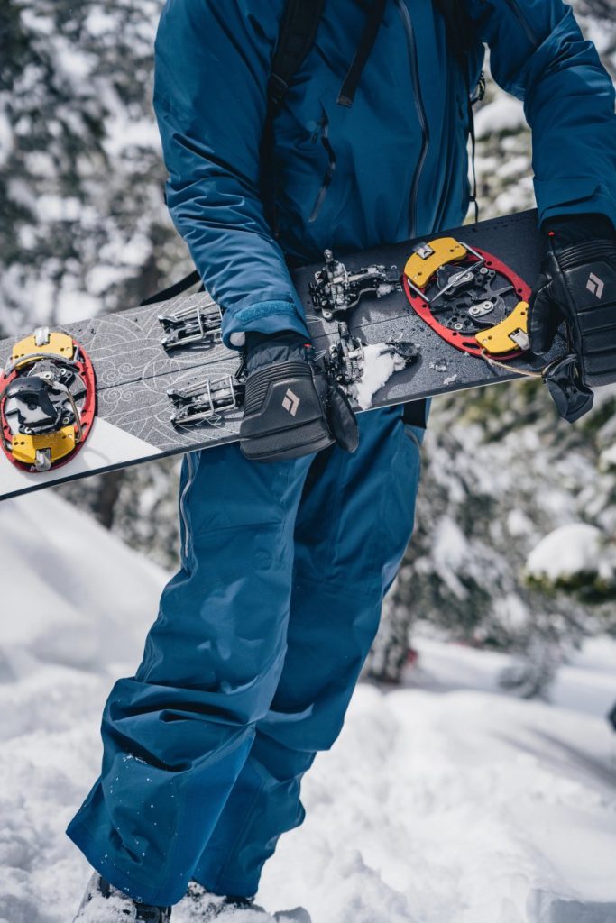 Mann im Schnee trägt Black Diamond Skihandschuhe Progressions Mitts und hält Splitboard fest