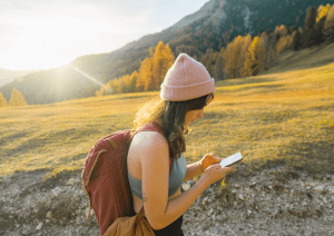 Wanderin mit Smartphone in der Hand auf einem sonnigen Bergpfad.