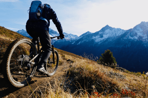 Mountainbiker fährt bergab auf einem Trail, dabei trägt er die 7mesh Glidepath Pant. Die Alpen im Hintergrund.