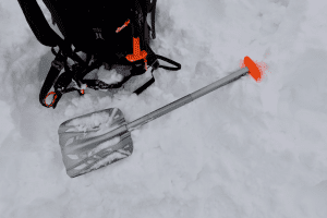 Mammut Alugator Ultra Schaufel liegt auf Schnee neben einem Rucksack.