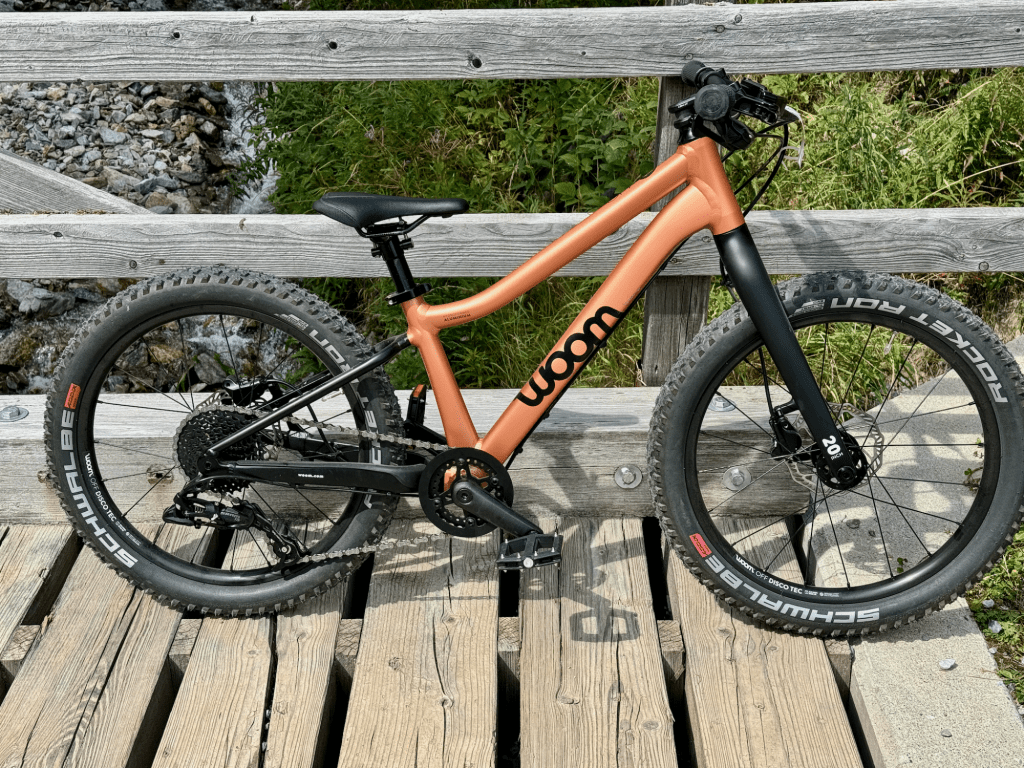 Das woom OFF 4 Kinder-Mountainbike steht auf einer Holzbrücke, präsentiert das elegante Design.